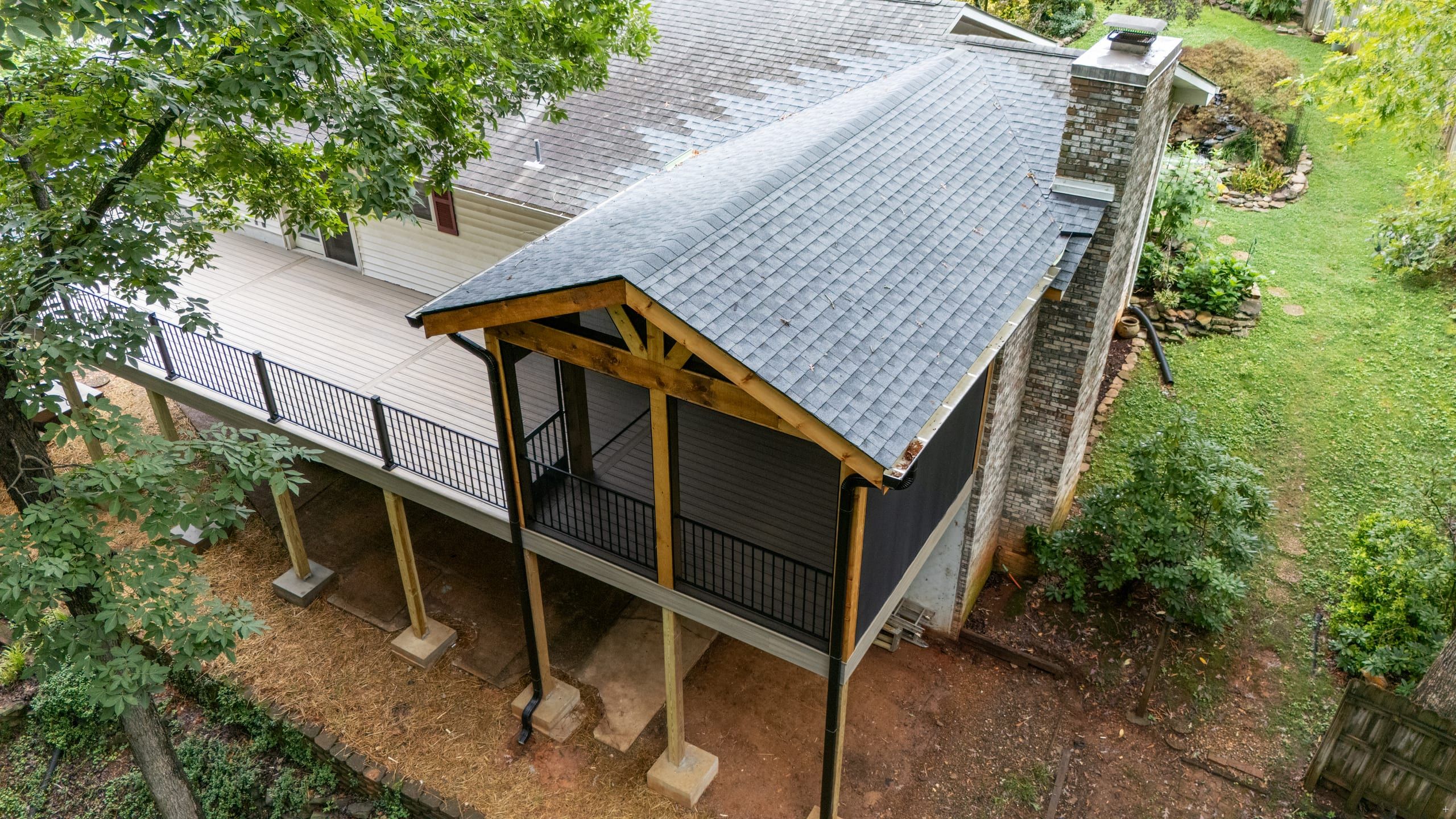 Aerial view of the Venice covered porch gable roof and elevated deck spanning the back of the home in a wooded lot