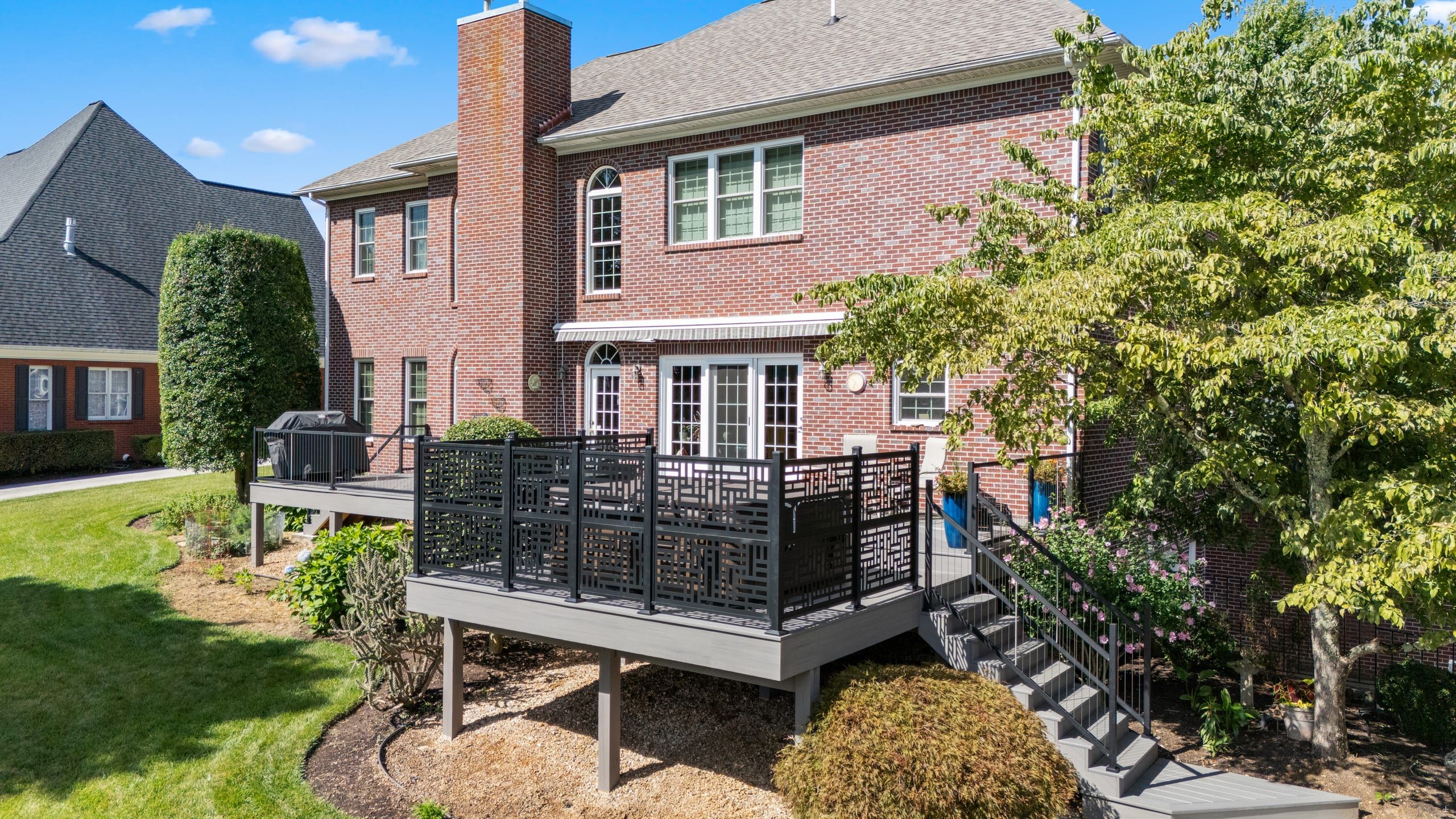 Elevated view of the Wilshire wraparound deck with black privacy screens and cable railing along a two-story brick home